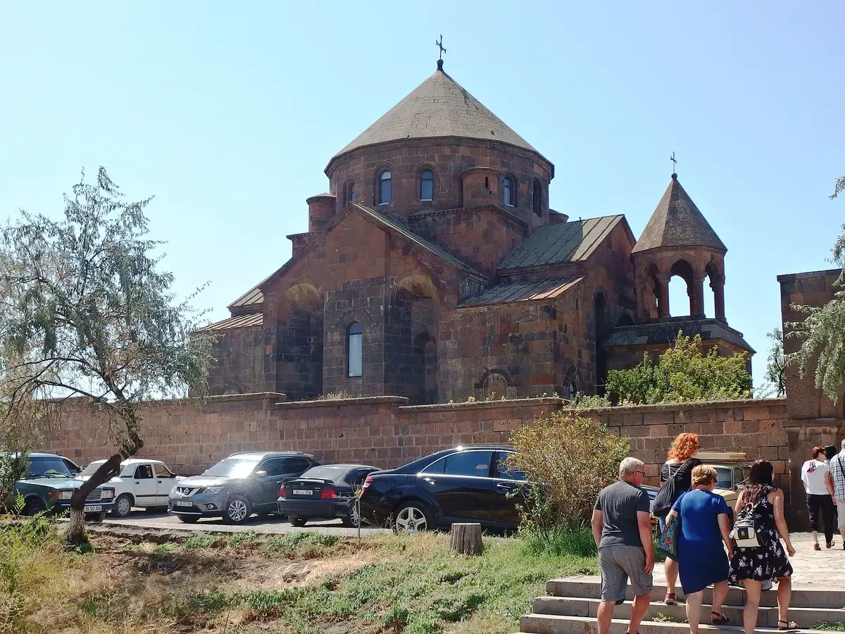 The tall stone facade and conical dome of Saint Hripsime Church against a blue sky in Vagharshapat