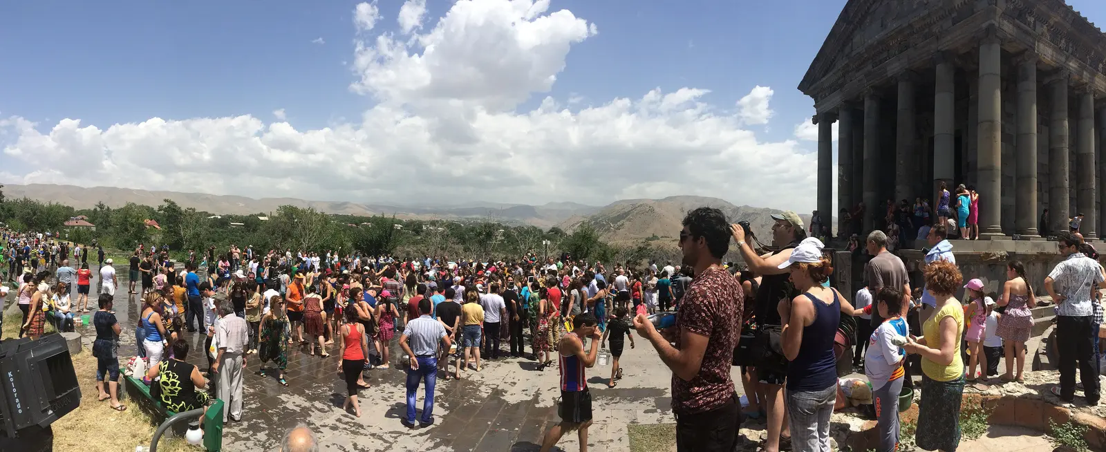 A large crowd gathered for Vardavar at the columns of the Garni pagan temple with mountains behind