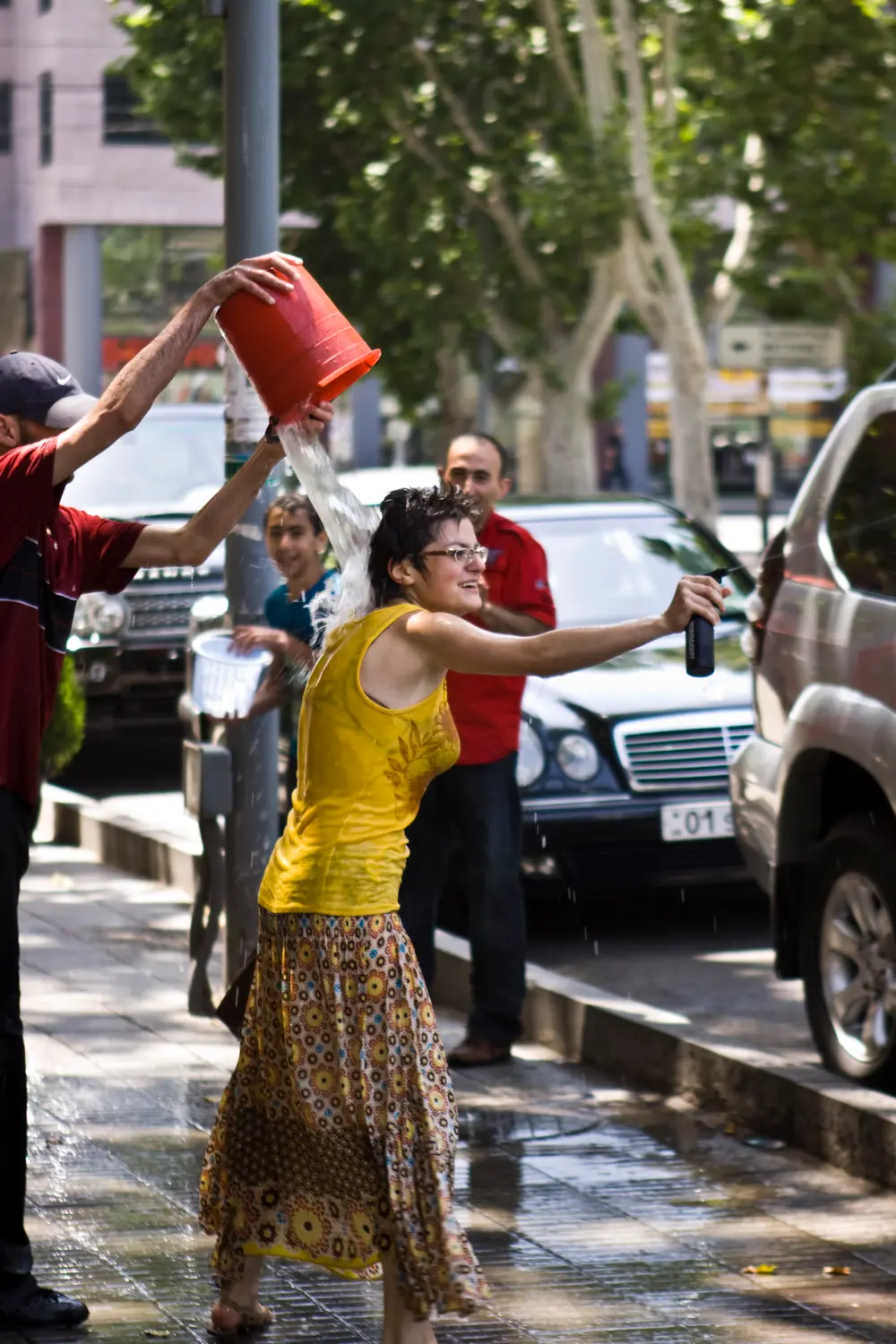 A man tipping a red bucket of water over a laughing woman who sprays back with a bottle on a Yerevan street