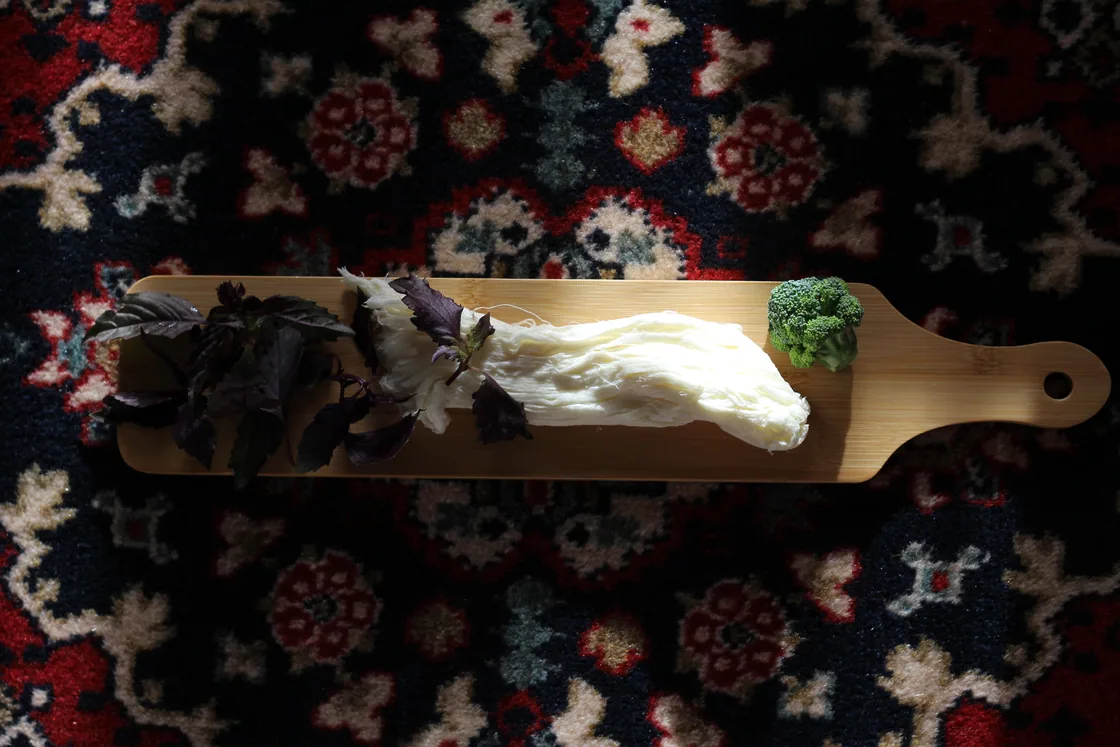 A rope of white braided chechil string cheese with fresh basil on a wooden board