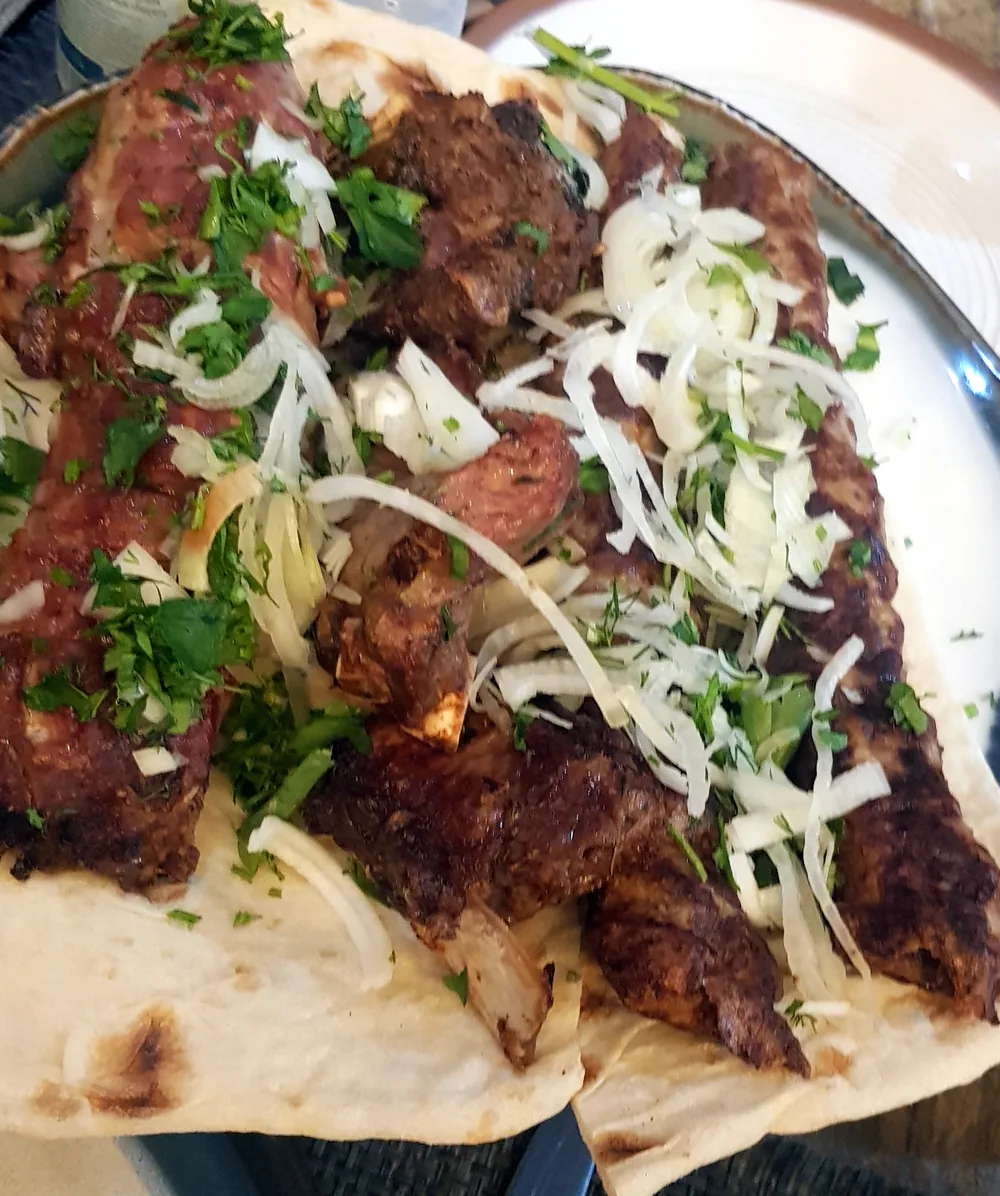 Skewers of khorovats grilling over a long outdoor mangal near stony ground