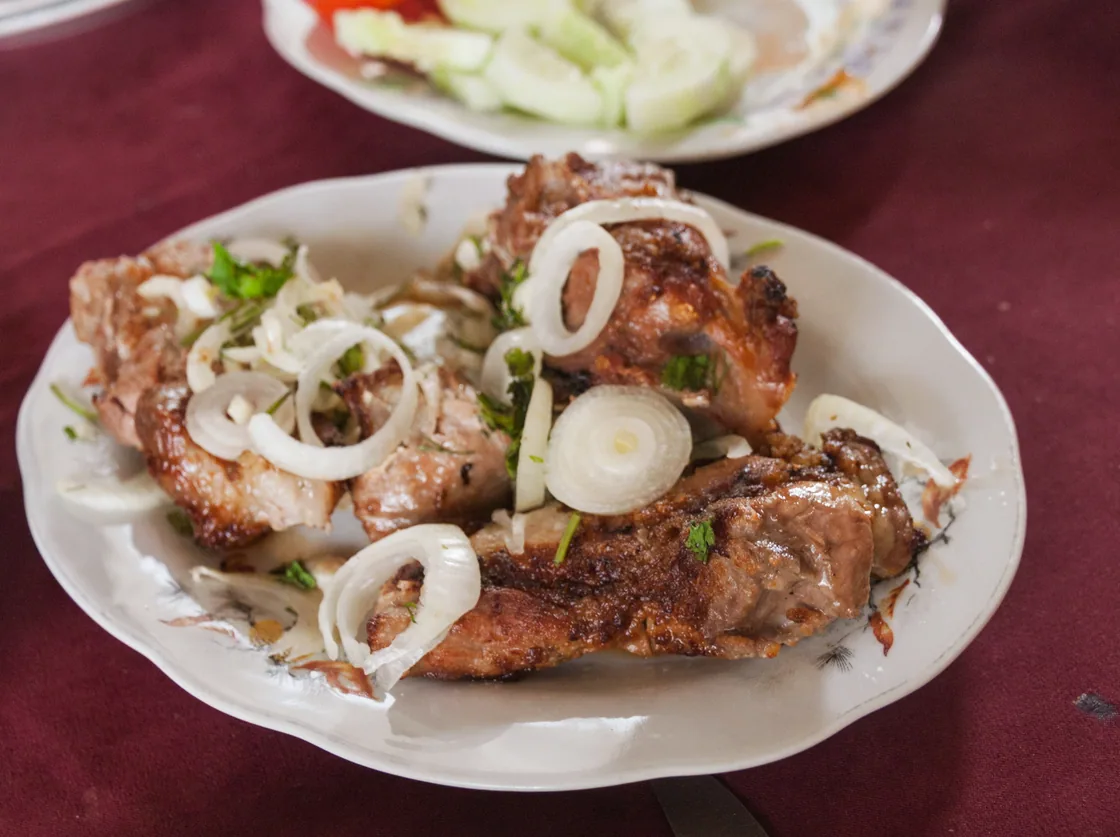 A plate of grilled khorovats pork topped with raw onion rings and herbs on a table