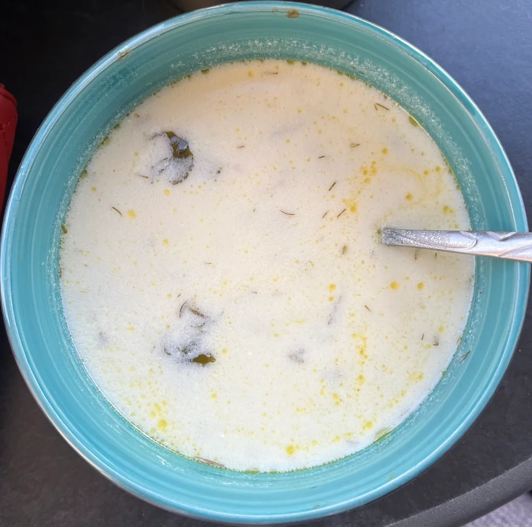 A bowl of spas, a creamy white Armenian yogurt soup flecked with herbs, with a spoon