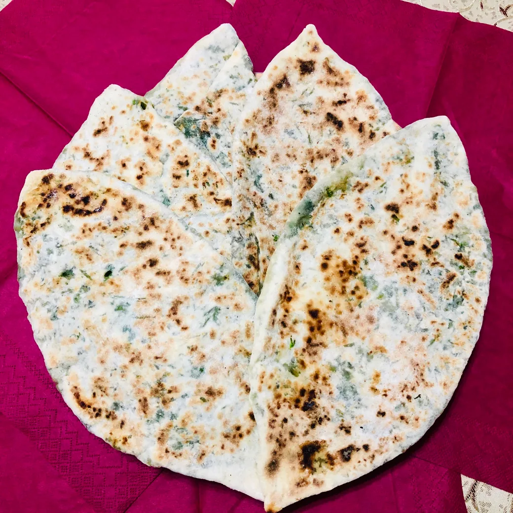 Griddled zhingyalov hats flatbreads stuffed with chopped greens, arranged on a pink cloth