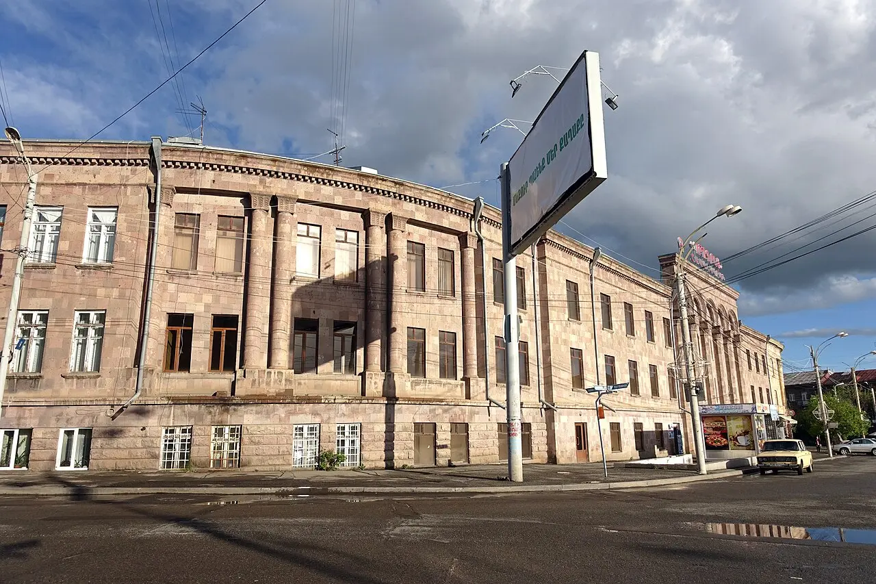 A grand curved neoclassical tuff building on a corner in central Gyumri under dramatic clouds