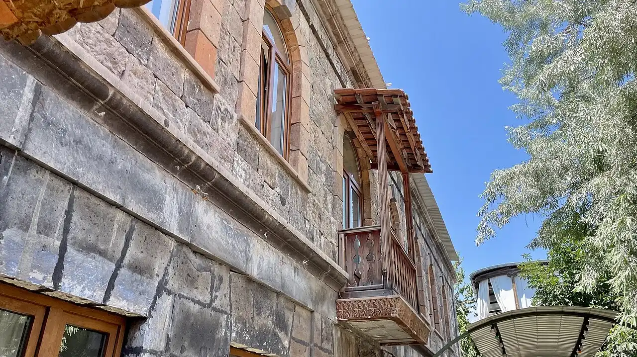 A restored 19th-century tuff mansion with a carved wooden balcony under a blue sky in central Gyumri