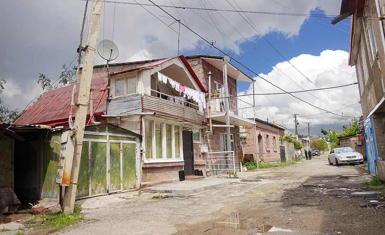 A two-storey tuff house with a wooden balcony and hanging laundry on a residential street in Gyumri