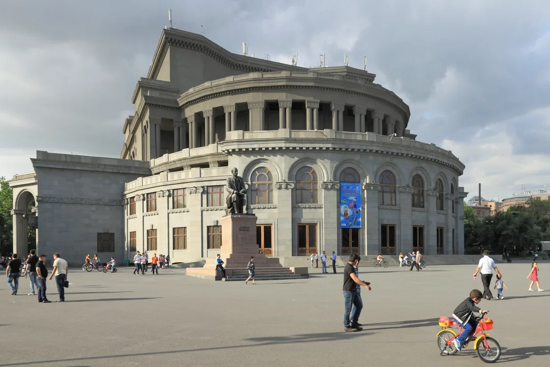 The rounded stone facade of the Yerevan Opera and Ballet Theatre surrounded by trees
