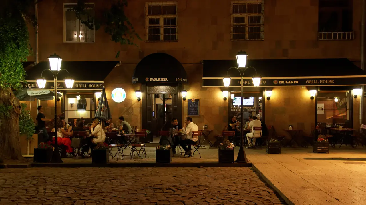A lantern-lit restaurant terrace filling up after dark on Tamanyan Square in central Yerevan