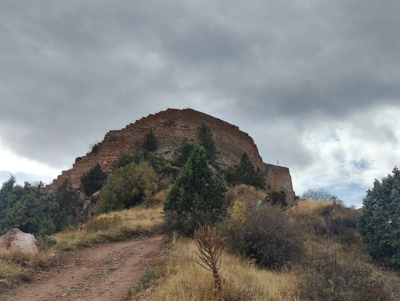 The stone ramparts of Smbataberd fortress crowning a ridge above the Yeghegis valley under a grey sky