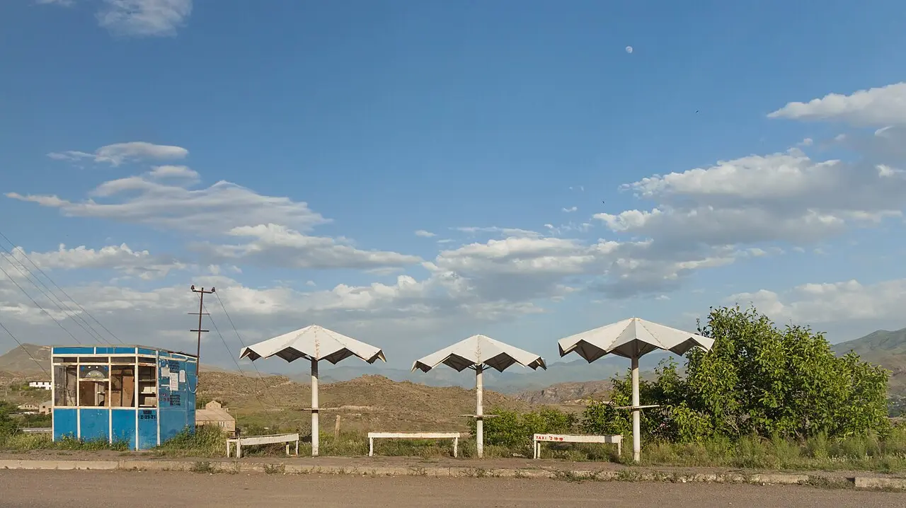Three white concrete umbrella shelters and a blue kiosk at a roadside stop near Yeghegnadzor