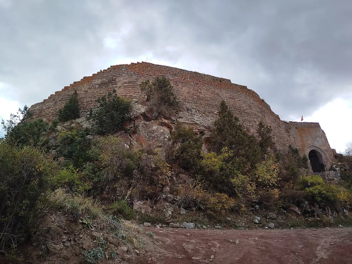The long stone rampart of Smbataberd fortress running along a rocky ridge under grey cloud