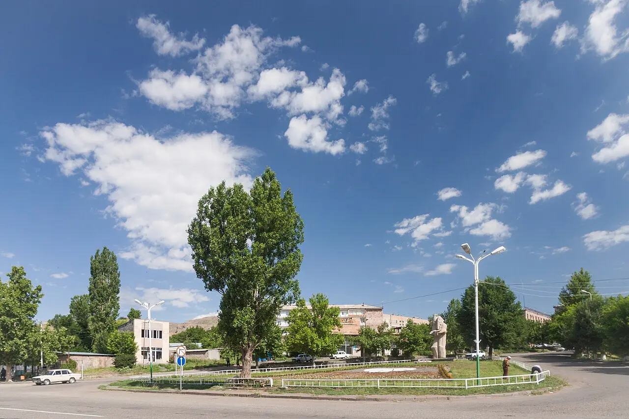 A quiet roundabout with a tall poplar and Soviet-era apartment blocks at the entrance to Yeghegnadzor