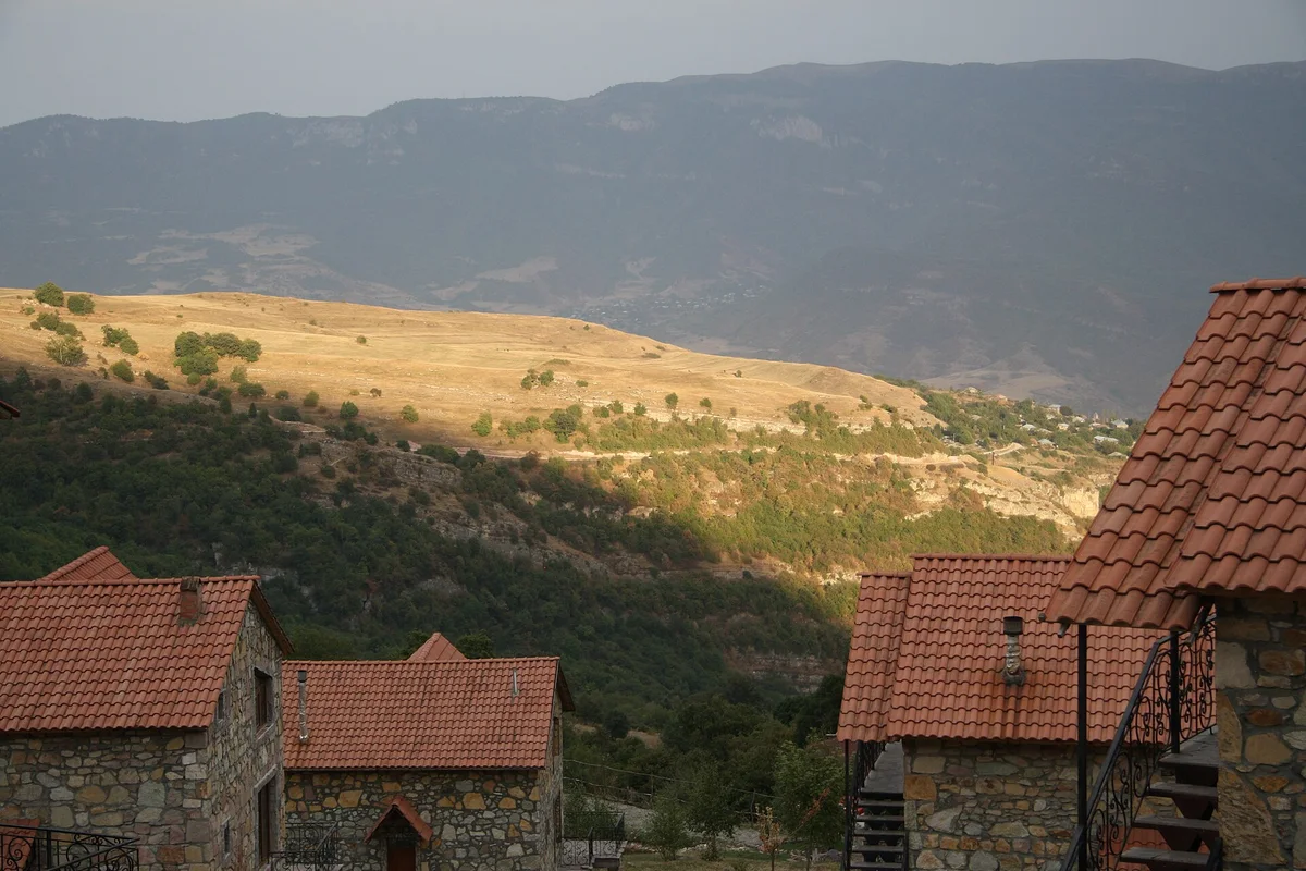 Stone cottages with red tiled roofs at Apaga Resort in Yenokavan, with the canyon and hills behind in evening light