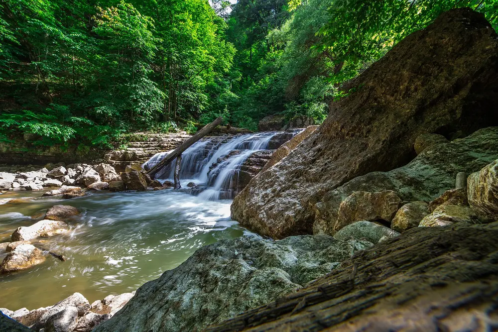 A wide cascade on the river at Lastiver spilling over rock ledges between mossy boulders and green forest