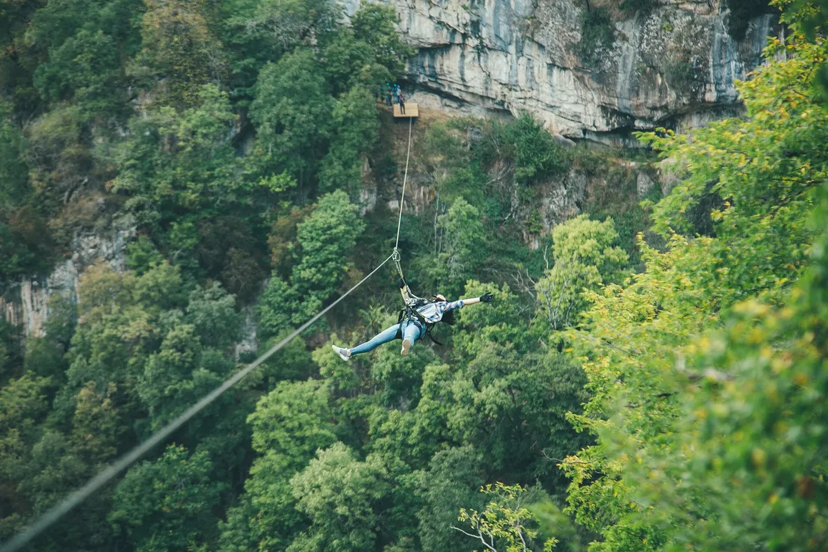 A zipline rider mid-flight below a wooden launch platform bolted into the cliff at Yenokavan