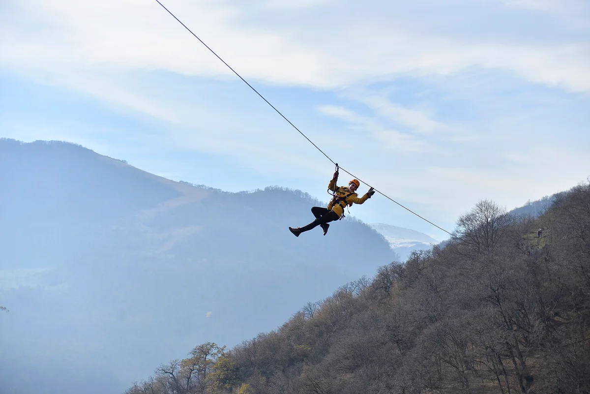 A lone zipline rider silhouetted on the cable above hazy blue ridges and bare winter forest at Yenokavan