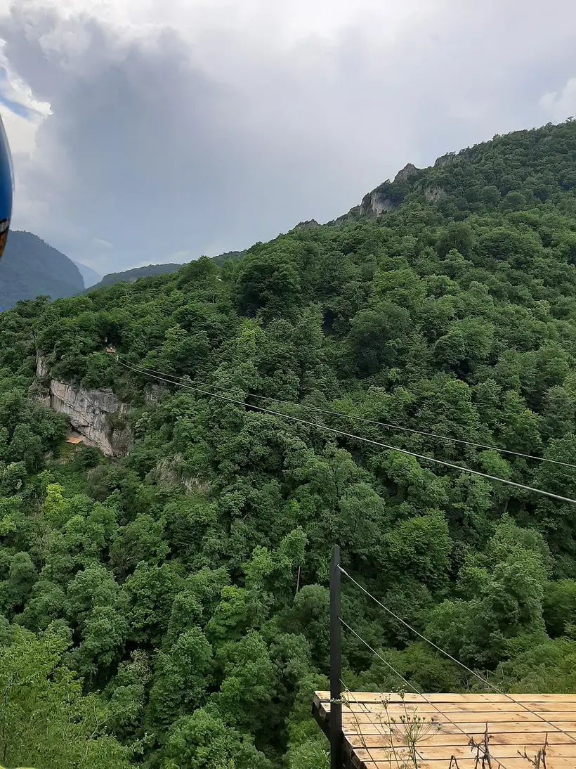 View from the wooden launch deck across the forested Yenokavan gorge with two zipline cables running to the cliff opposite