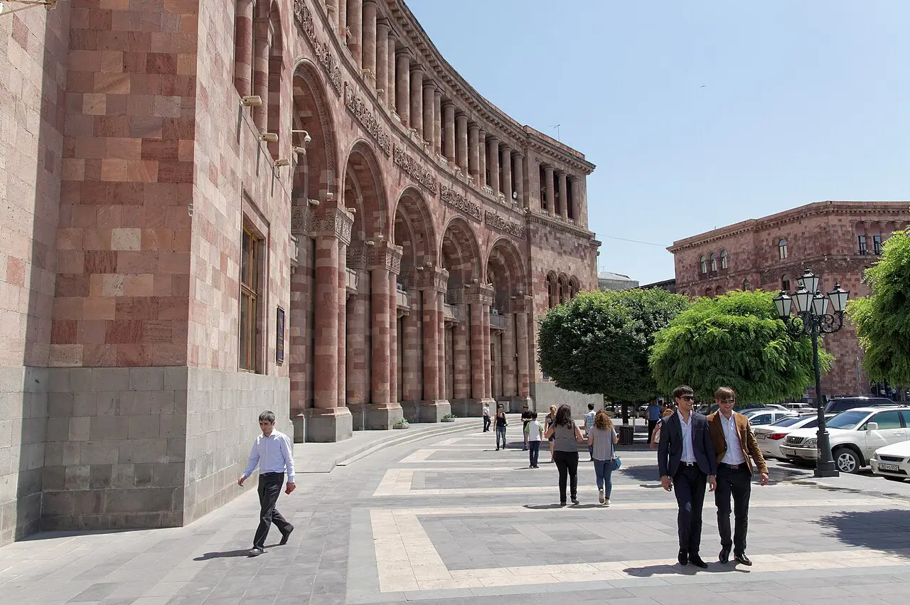 People walking across the pink-tuff paved Republic Square in central Yerevan past the arcaded government buildings on a sunny day