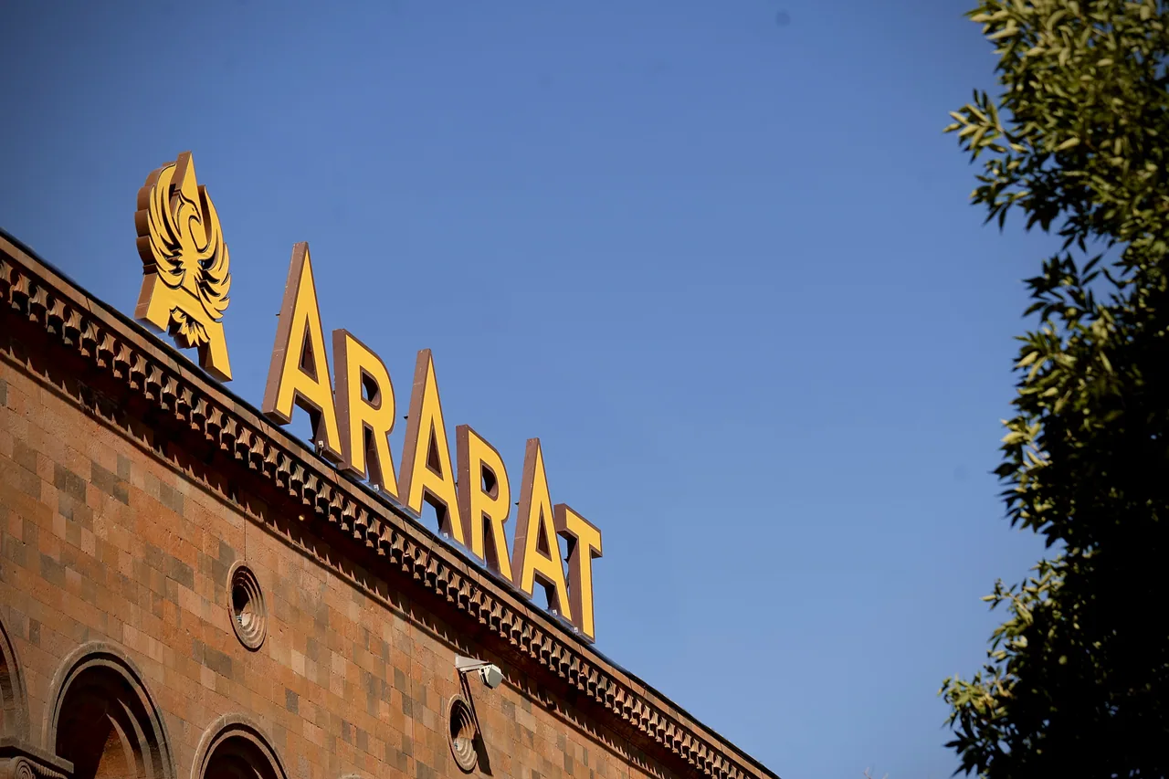 The golden ARARAT wordmark and winged logo on the tuff-brick facade of the Yerevan Brandy Company against a blue sky