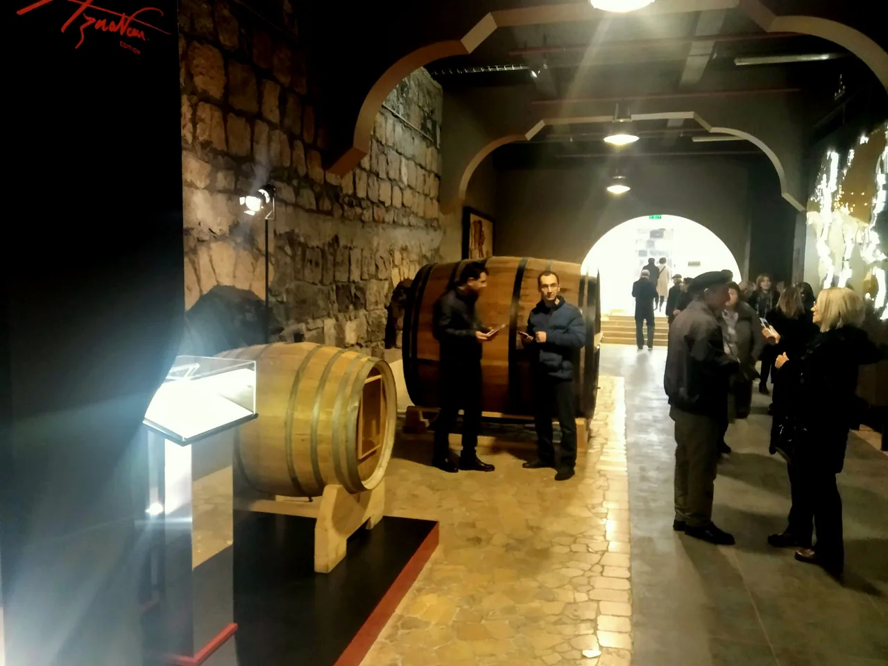 A hall in the Ararat museum with a wall of framed black-and-white photographs of famous visitors above a group of guests