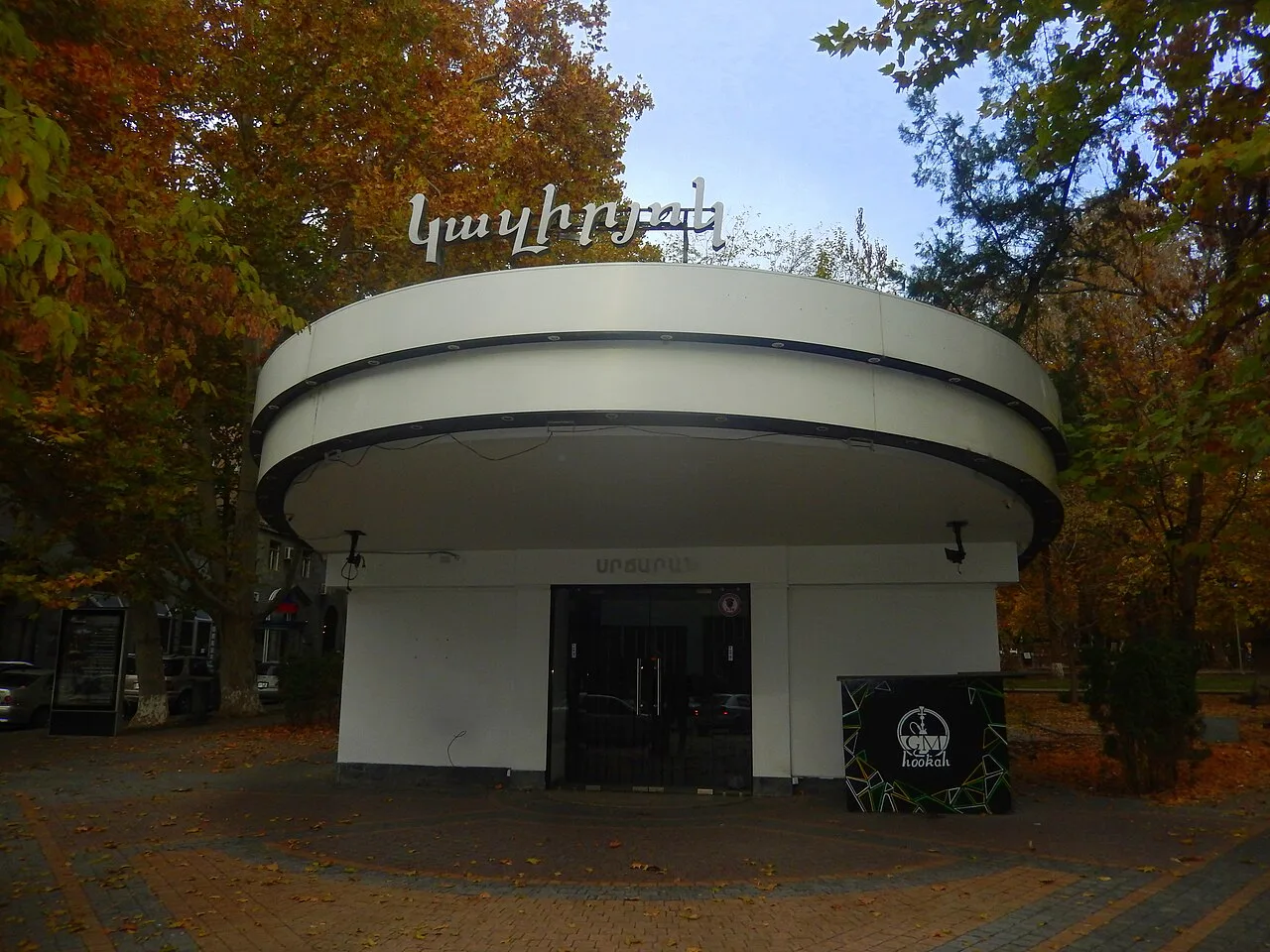 The round pavilion exterior of a Yerevan cafe among autumn trees, with a dark entrance and a hookah lounge sign beside it