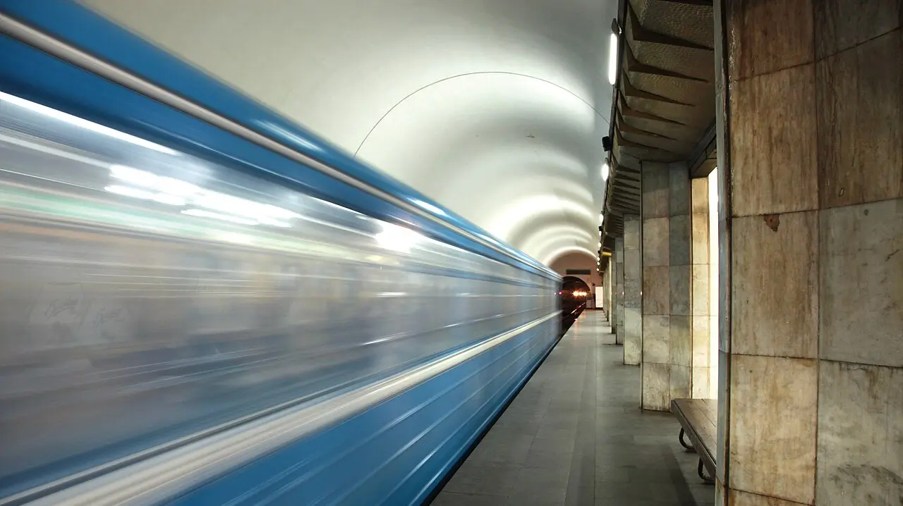 A blue metro train rushing into a marble-clad, barrel-vaulted platform on the Yerevan Metro