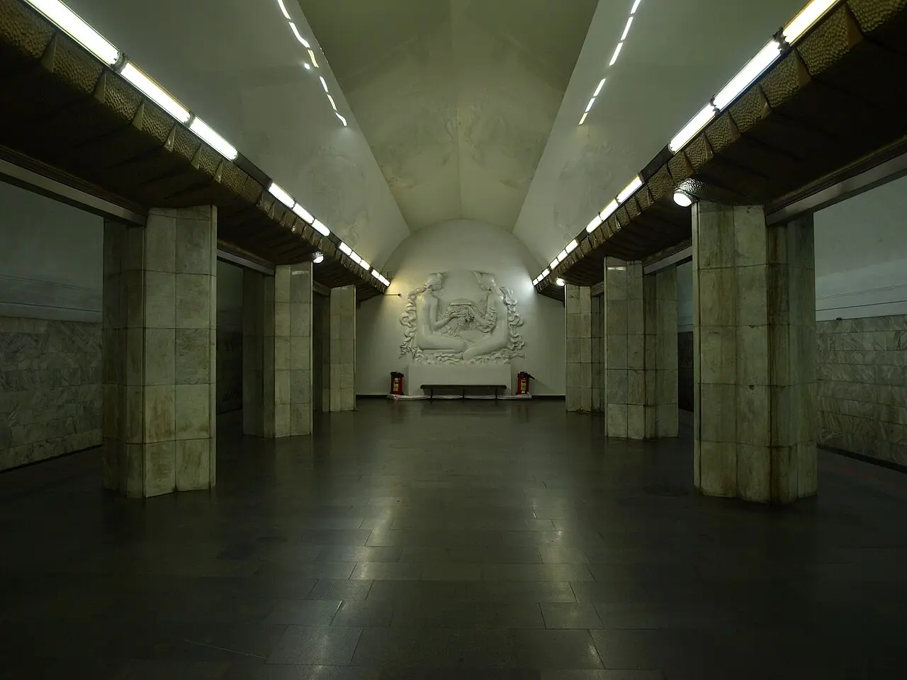 An empty Yerevan Metro station hall with marble columns, a barrel-vaulted ceiling and a white bas-relief on the far wall