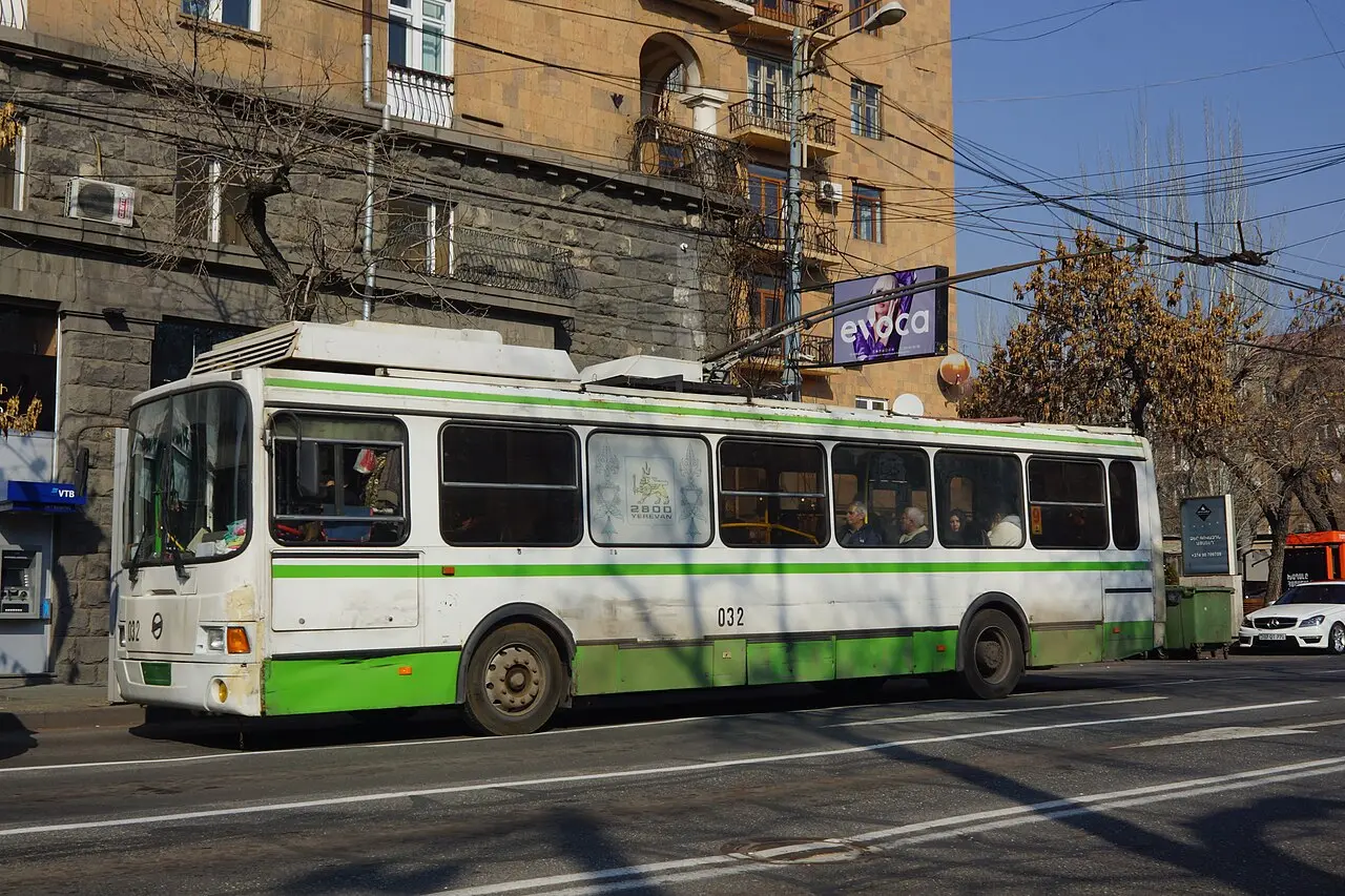 A white and green trolleybus number 032 running under overhead wires on a central Yerevan street