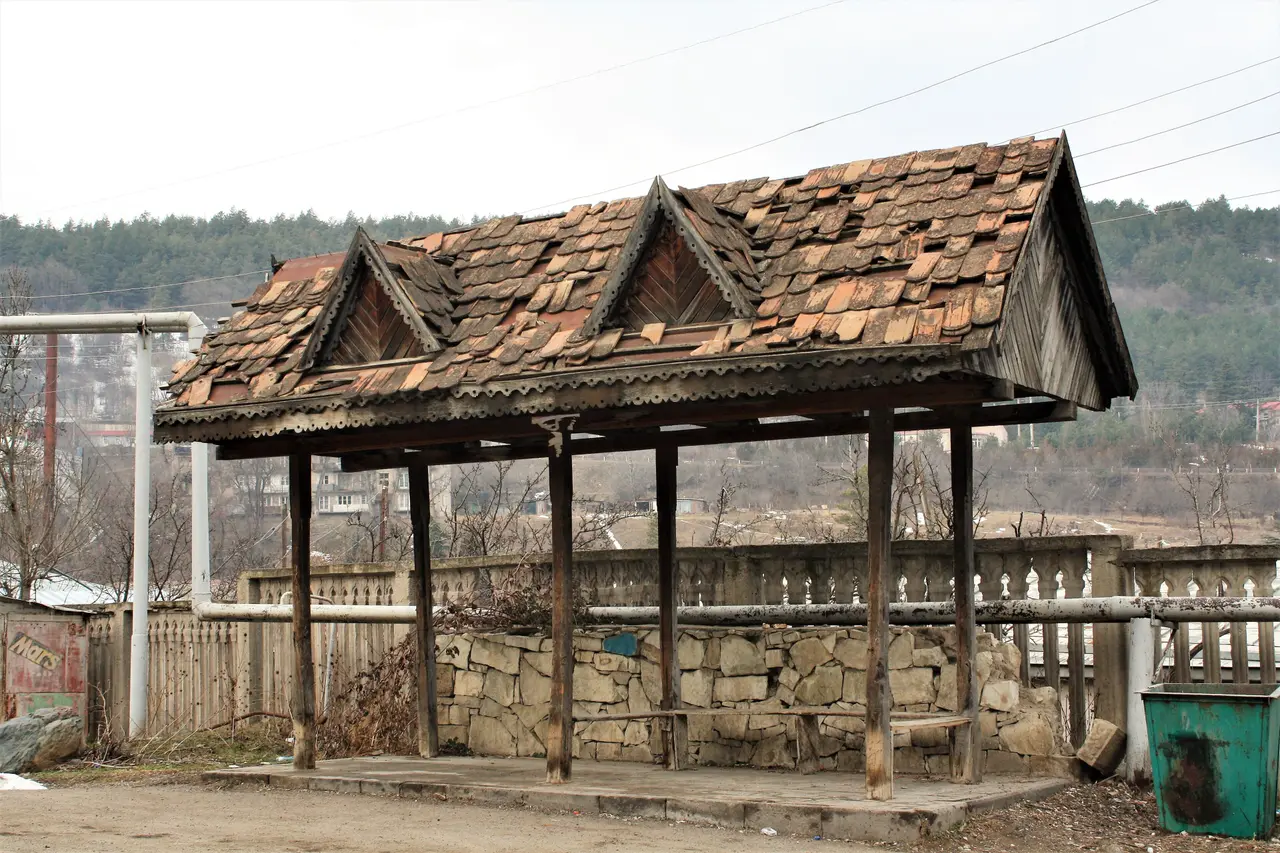 An old wooden-roofed bus shelter with a tiled roof in Dilijan, forested hills behind