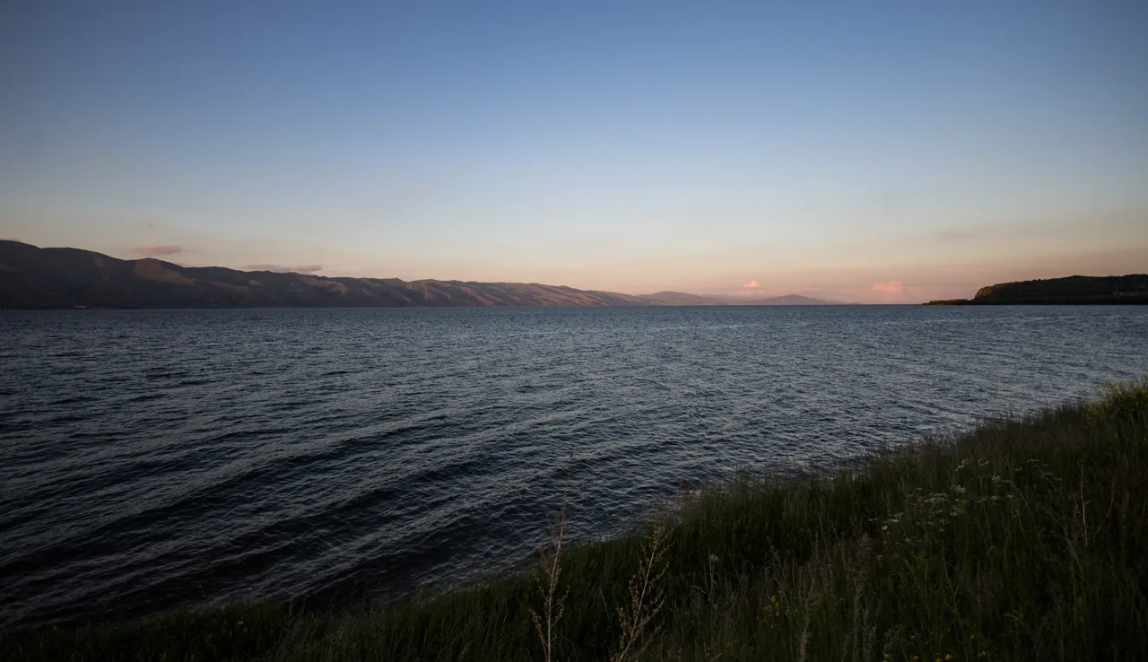 Lake Sevan under a bright sky with the surrounding ridges reflected in the calm water