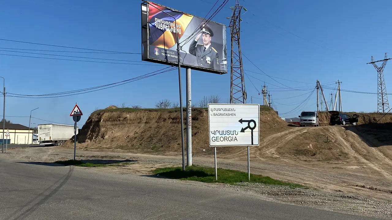 Blue and white road signs at the Armenia-Georgia border crossing in Bagratashen, one pointing back toward Yerevan