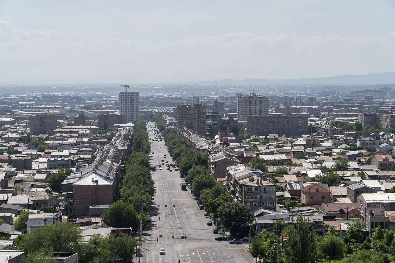 A wide view over central Yerevan from the hill of the Erebuni fortress, low pink-tufa blocks spreading toward the hills