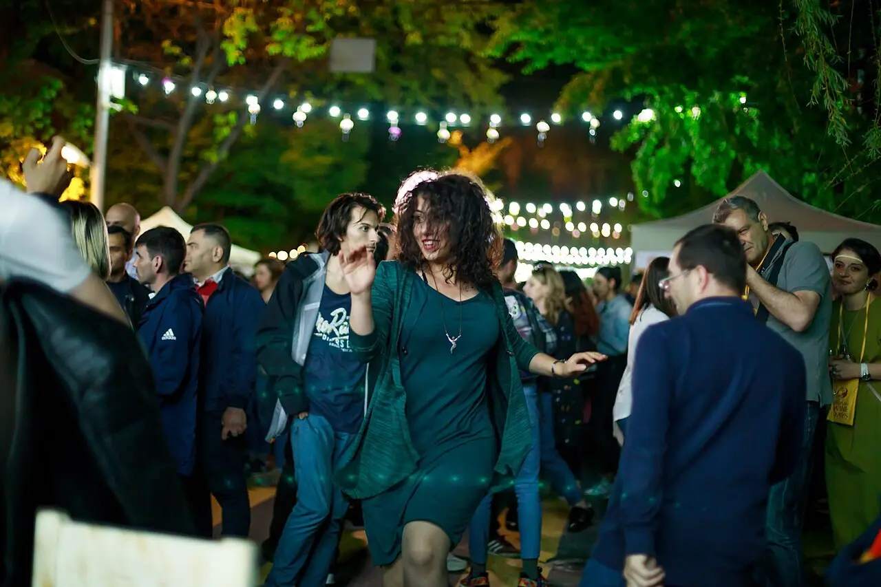 Festival-goers laughing and holding wine glasses among outdoor stalls